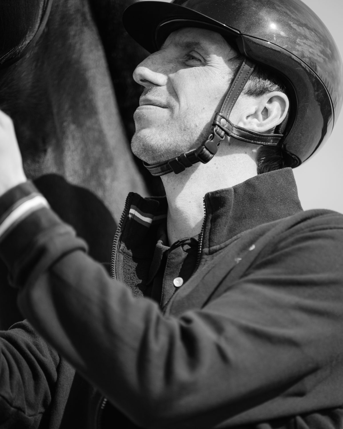 Antoine in profile beside a dark horse, helmet on, in black and white