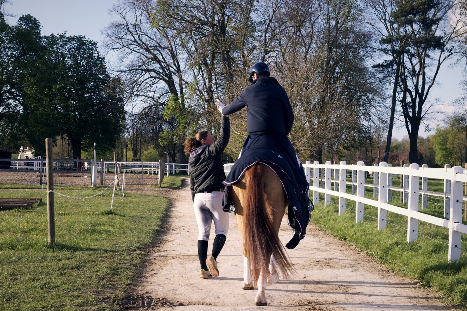 A rider and groom walking a rugged horse home after work, late light
