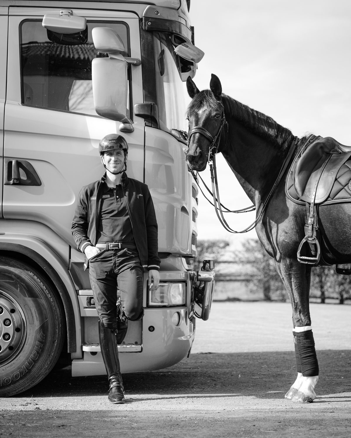 Antoine standing with a saddled horse beside the lorry, in black and white